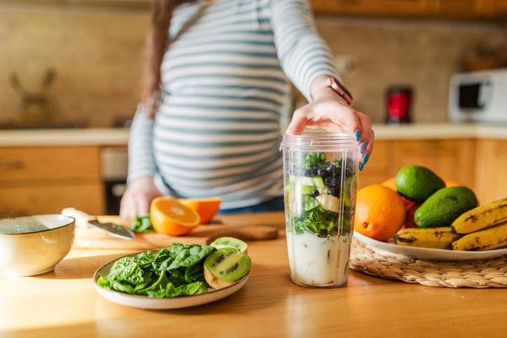 A pregnant woman eating a salad and preparing a green smoothie