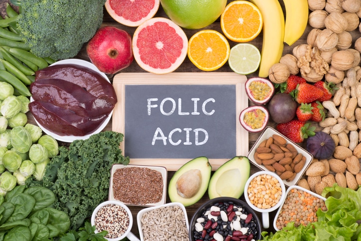 An assortment of fruits, vegetables, and nuts surrounding a sign that says "FOLIC ACID"