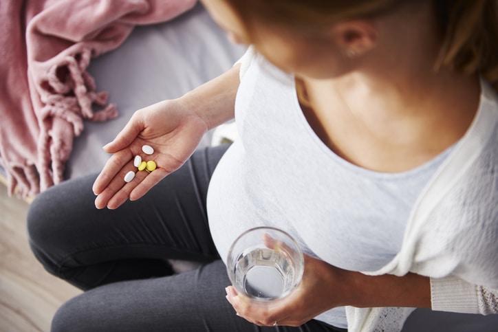 A pregnant woman holding five pills in her palm