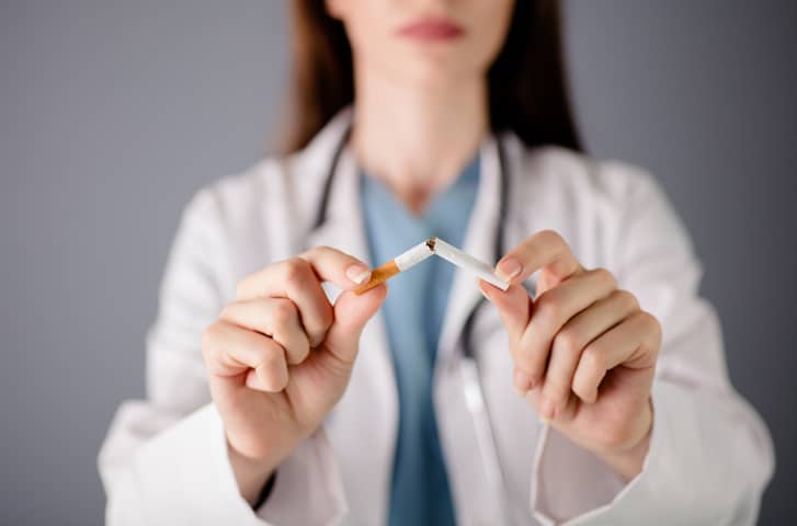 A stock image of a medical provider in a white coat ripping a cigarette in half in front of the camera