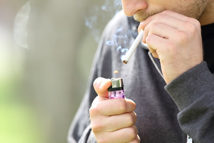 A man lighting a cigarette with a purple BIC lighter