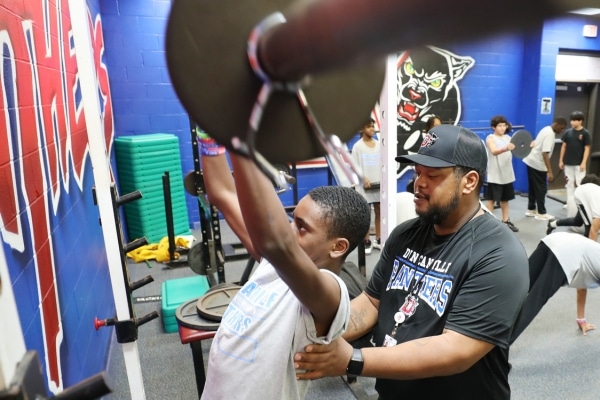 Tremont Davis, a football coach, helping a young athlete lift weights