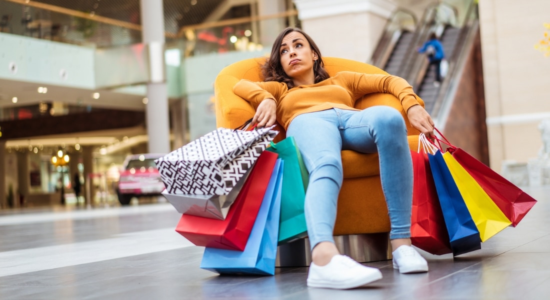 An exhausted woman with many shopping bags takes a break in a shopping mall.