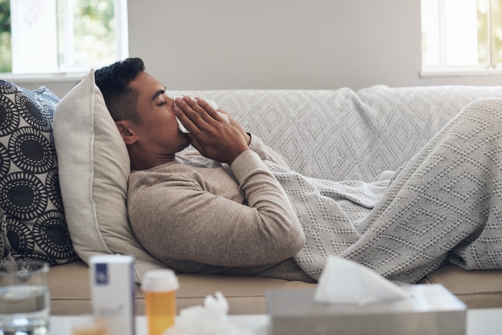 Young man blowing his nose while feeling sick at home