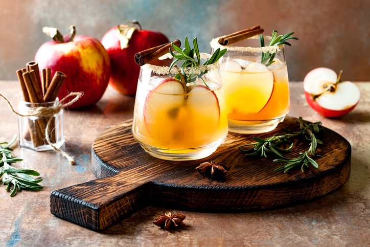 Fall-inspired beverages staged with a wooden serving tray, cinnamon sticks, apples, and rosemary
