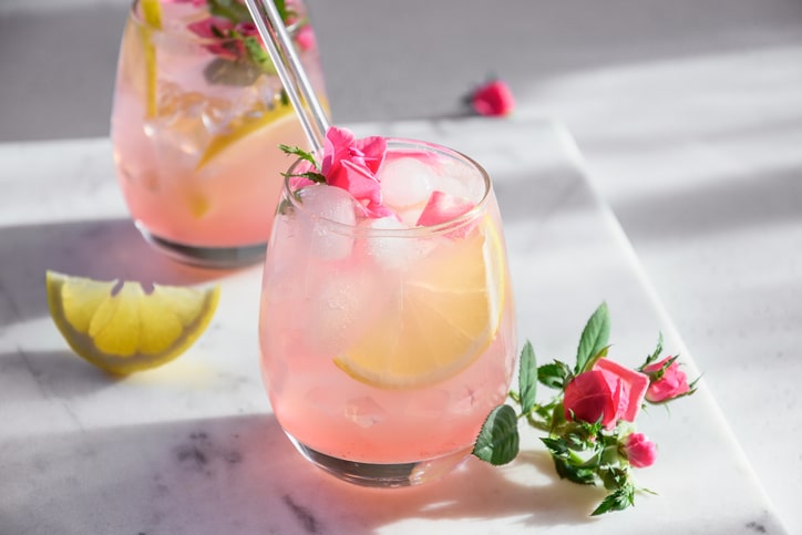 A fruity, pink beverage in a clear glass, staged with lemon wedges and pink flowers