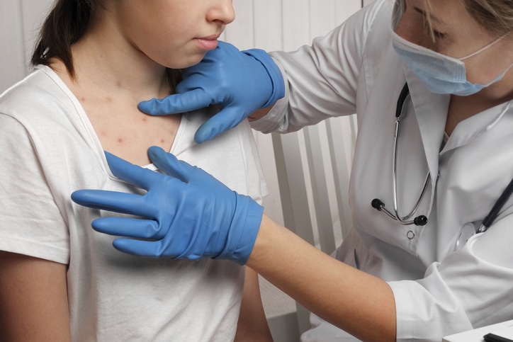 A medical provider examines a rash on a young woman's chest.