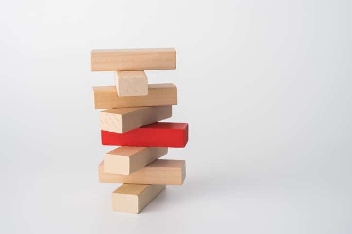Eight building blocks form a tower. One of the central blocks is red; the rest are natural wood color.