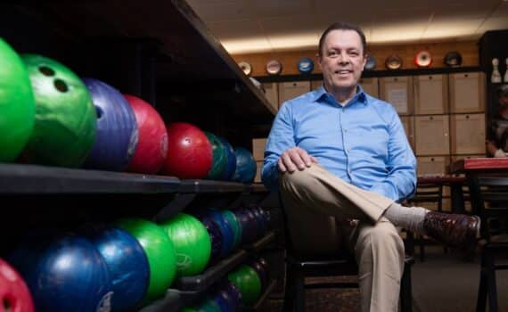 Bowler James Wann photographed next to two rows of bowling balls after surviving a heart attack