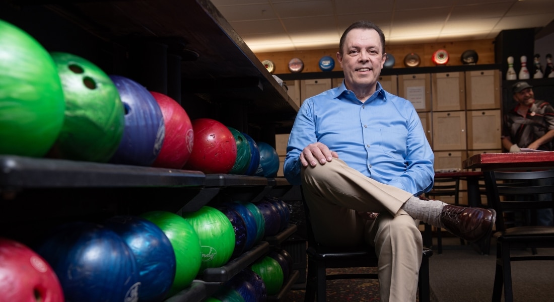 Bowler James Wann photographed next to two rows of bowling balls after surviving a heart attack