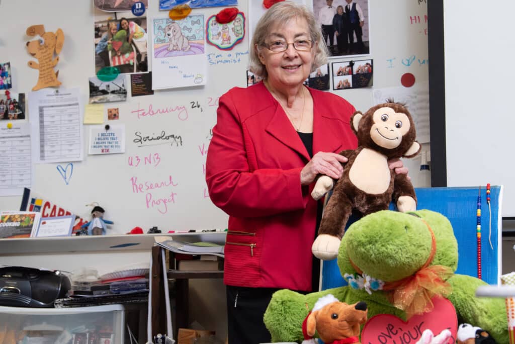 Eugenia Jameson holding a monkey stuffed animal in front of a white board in a classroom