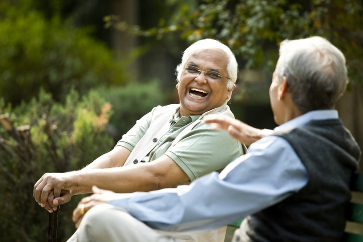 Two older adults looking at each other and laughing while sitting together on a bench