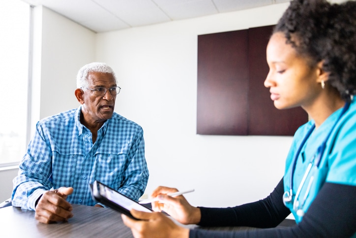 An older adult man speaking with a medical provider while sitting at a table.