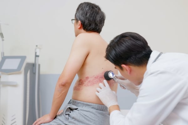A medical professional inspecting a rash on an older man's middle back.