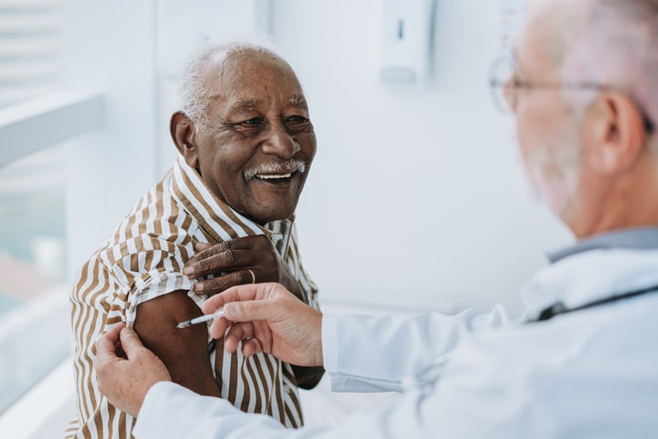 An older man receiving a vaccine from a medical professional and smiling at the provider.