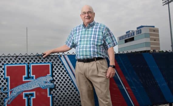 Bill Burdett smiling in front of a high school logo, used to explain his surgery for multiple hernias