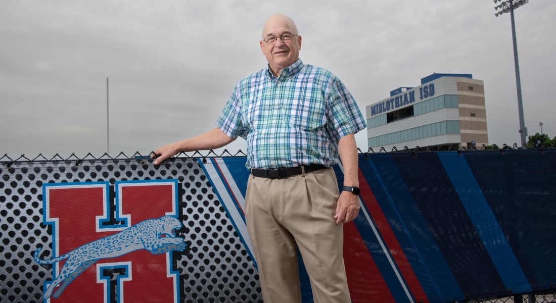 Bill Burdett smiling in front of a high school logo, used to explain his surgery for multiple hernias