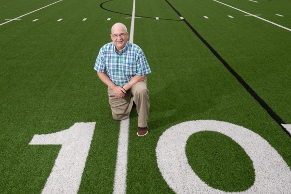 Bill Burdett taking a knee near the 10 yard line on a football field at a Midlothian ISD school