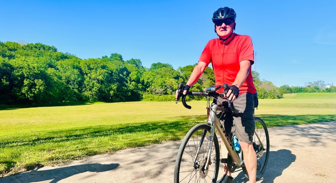 Ed Ofria photographed in a red shirt and black activewear shorts while riding his bike, used to explain his new hip replacement surgery