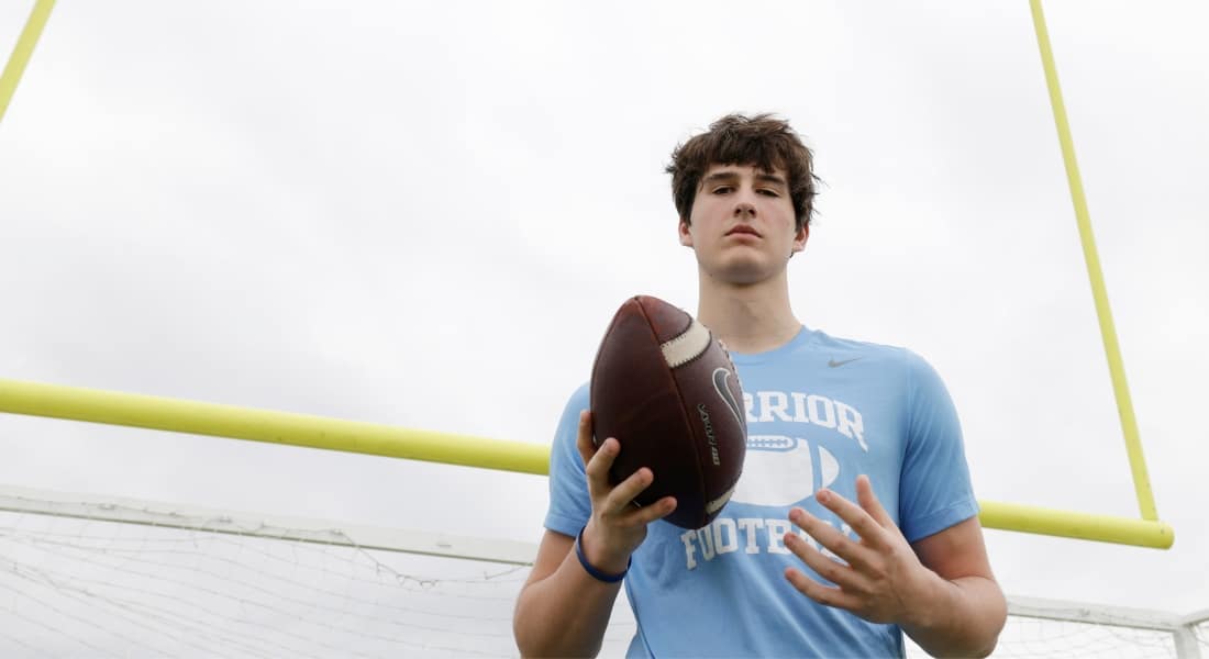 Liberty Christian wide receiver Henri DeRoche photographed wearing a school football shirt and holding a football in front of his body