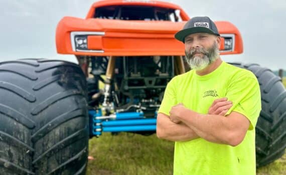 A man named Shane England standing in front of an orange monster truck, used to explain his recovery after a widow maker heart attack