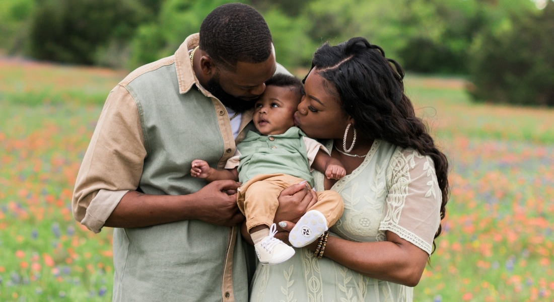 LaTeisha Young, her husband Jeromey, and their newborn Mason photographed outside in an editorial or portrait style while wearing green and brown complementing outfits, leaning in and looking at their baby, used to explain LaTeshia's IVF journey with Methodist Midlothian