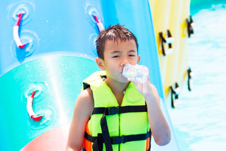 A boy wearing a life vest drinks from a bottle of water.