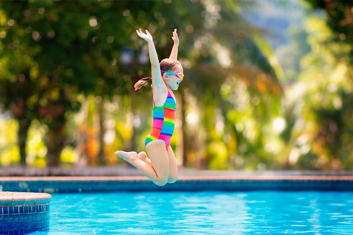 A girl in a bright swimsuit jumps into a swimming pool.