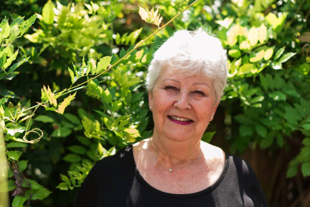 A woman named Wendy Aschner photographed smiling in front of green bushes