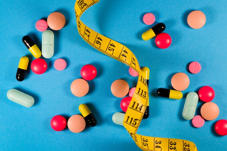 A tape measure winds between colorful pills against a blue background.