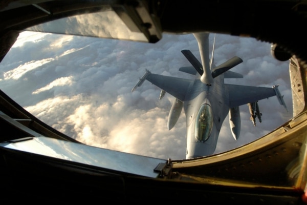 A KC-135 Stratotanker refuels an F-16 over clouds lit from above with sunlight.