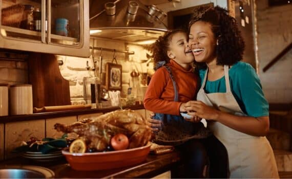 A daughter gives her mother a kiss in the kitchen next to the Thanksgiving turkey