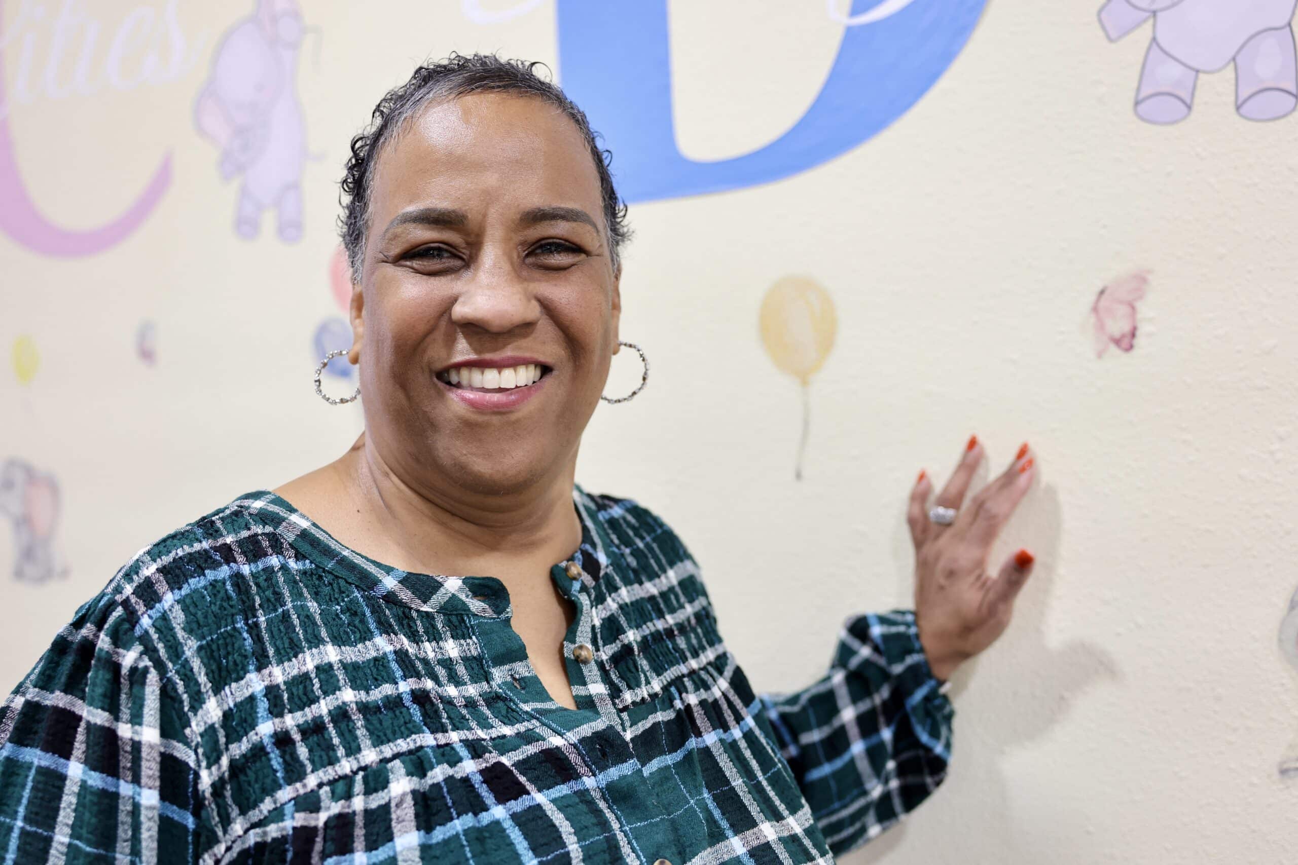 A woman named Karol Fuget poses for a photo by leaning on the wall in the daycare she runs.