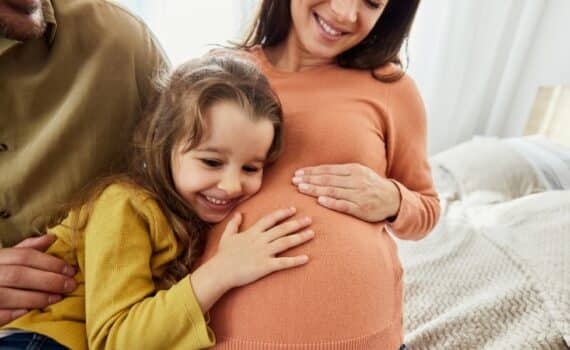 Little girl listening to her pregnant mother's belly as father looks on.