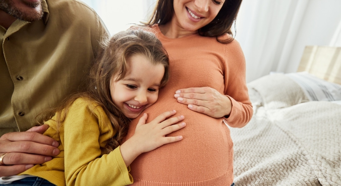 Little girl listening to her pregnant mother's belly as father looks on.