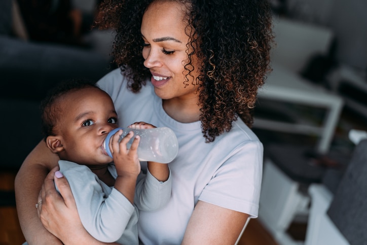 Mother feeds her baby boy with baby milk.