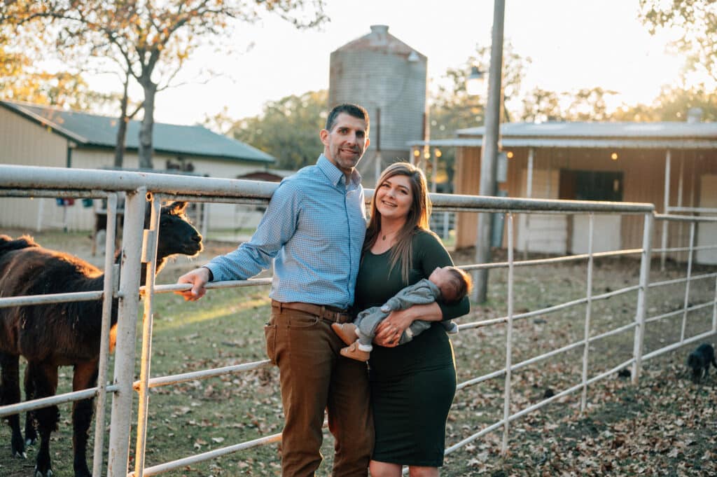 Michael Farrah stands beside a llama corral with his wife, Jessica, holding their new baby, Miles.