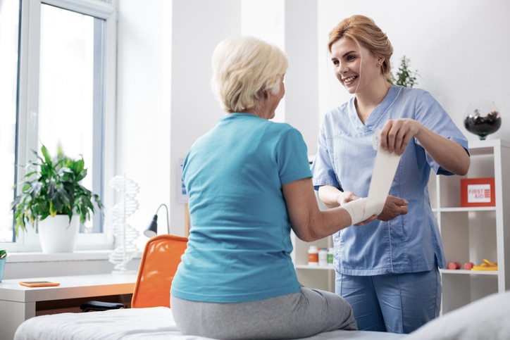 Friendly female nurse smiling as she wraps a patient's wound in the hospital