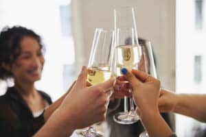 Cropped shot of friends hands toasting with champagne flutes. Close-up of group of people celebrating and toasting wine glasses during dinner party at home.