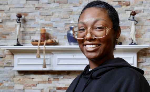 Kiana Hill poses in front of her fireplace mantle with a smile.