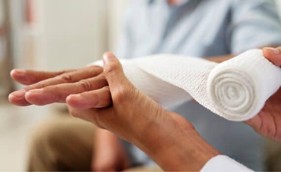 Close-up of nurse holding and bandaging hand of senior patient at hospital