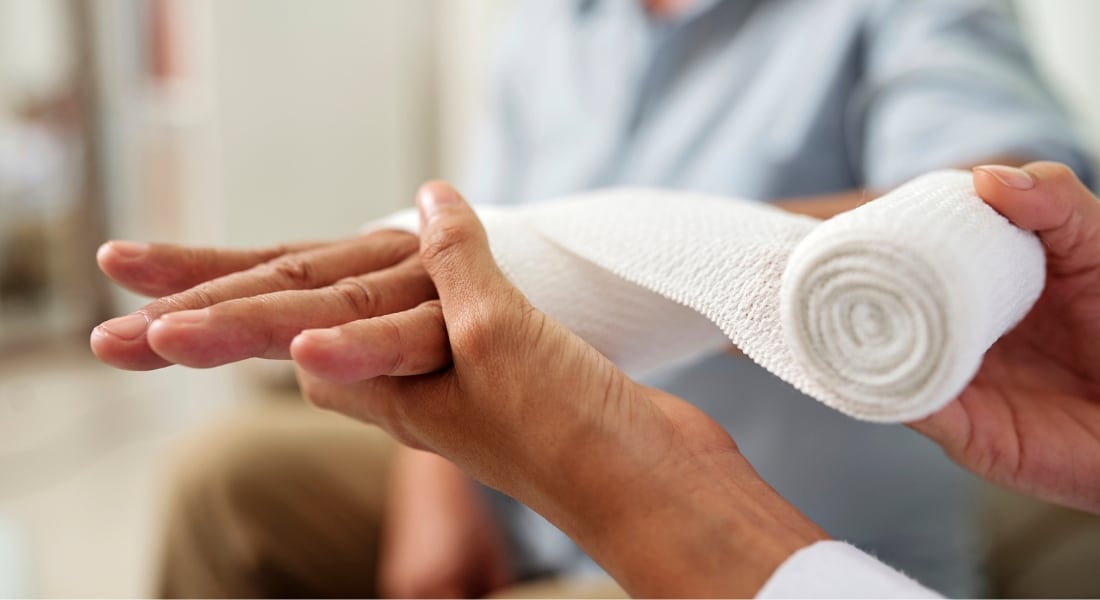 Close-up of nurse holding and bandaging hand of senior patient at hospital