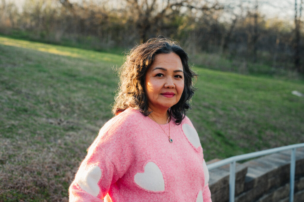 Kout Aun poses outside wearing a pink shirt with white hearts.