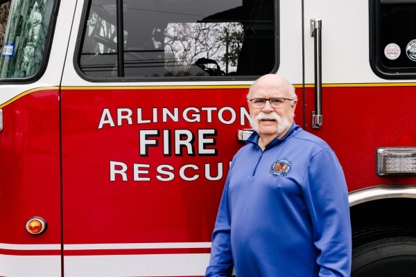 Retired firefighter stands beside a firetruck at his old firehouse.