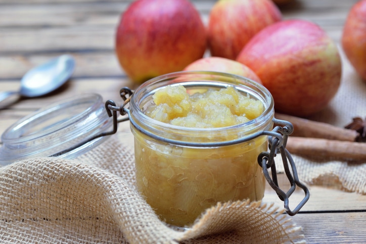 Applesauce in a glass jar with red apples in the background