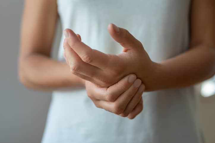 A young woman massages her hand while suffering from arthritis pain.