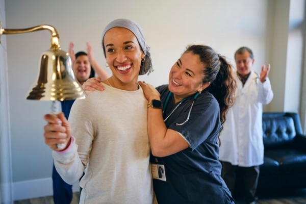 A nurse hugs a chemotherapy patient as she rings a bell signifying the end of her treatment.