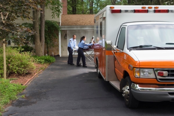 A paramedic crew wheels a patient our of a home to a waiting ambulance.
