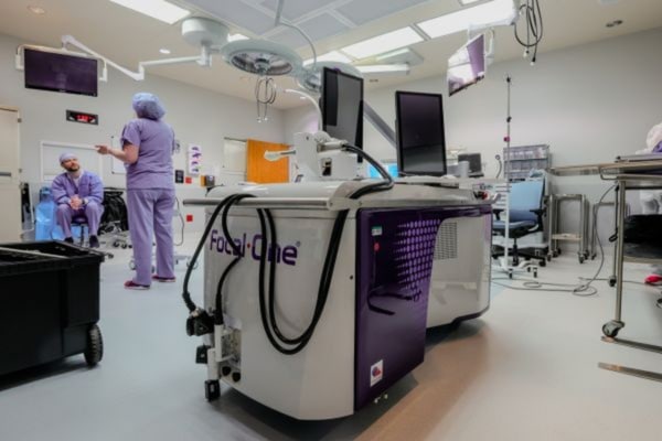 Clinical staff talk in an operating room beside the Focal One HIFU Robotic System.