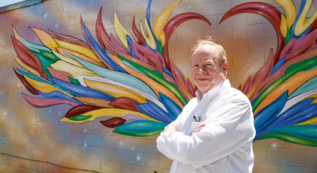 Heart attack survivor stands beside a heart mural in downtown Mansfield.